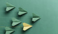 One yellow paper plane is flying on green background among a group of green paper planes. Representing individuality.