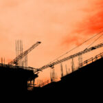Residential building development and construction, back lit cranes and scaffold with orange sky