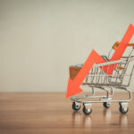 Shopping trolley with red chart falling down on wooden table white wall background copy space. Economic recession crisis, core retail sales decrease, inflation or goods price up concept.