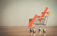Shopping trolley with red chart falling down on wooden table white wall background copy space. Economic recession crisis, core retail sales decrease, inflation or goods price up concept.