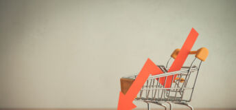 Shopping trolley with red chart falling down on wooden table white wall background copy space. Economic recession crisis, core retail sales decrease, inflation or goods price up concept.