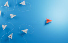 Paper planes, white flying randomlly but for one in red flying with purpose