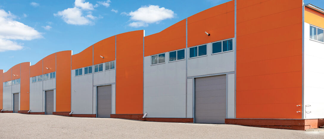 Photo of big, modern industrial warehouses with orange facades and rising gates, representing warehouses, logistics center or other commercial real estate.