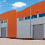Photo of big, modern industrial warehouses with orange facades and rising gates, representing warehouses, logistics center or other commercial real estate.