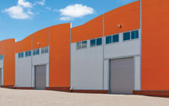 Photo of big, modern industrial warehouses with orange facades and rising gates, representing warehouses, logistics center or other commercial real estate.