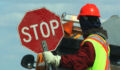 Side View Of Male Worker Holding Stop Sign Against Vehicle On Road