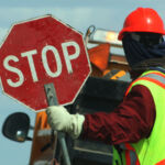 Side View Of Male Worker Holding Stop Sign Against Vehicle On Road
