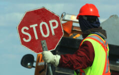Side View Of Male Worker Holding Stop Sign Against Vehicle On Road